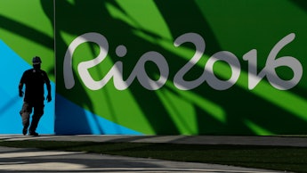 A man standing next to a green-blue-white wall with the text 'Rio 2016' for the Rio Olympics 2916