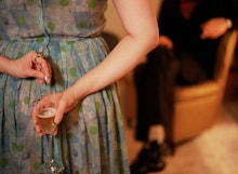 A woman putting a pill in a glass of champagne behind her back
