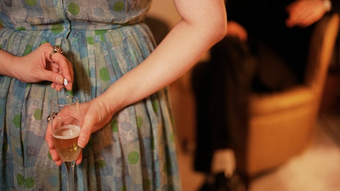 A woman putting a pill in a glass of champagne behind her back