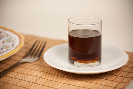 A glass of agave on a ceramic plate sitting on a bamboo table cover