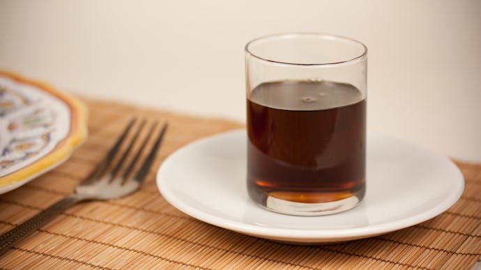 A glass of agave on a ceramic plate sitting on a bamboo table cover