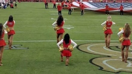 A group of NFL cheerleaders kneeling on a stadium
