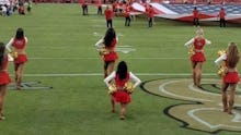 A group of NFL cheerleaders kneeling on a stadium