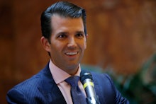 Donald Trump Jr. smiling while standing in front of a microphone at a political rally