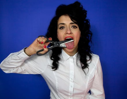 A female photographer's artwork where a woman in a white shirt cuts her tongue with a pair of scisso...