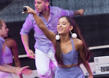 Ariana performing live in a purple dress as her dancers perform behind her