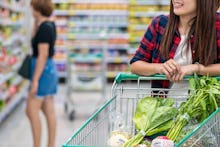 A woman leaning onto a shopping cart filled with $30 worth of groceries and veggies