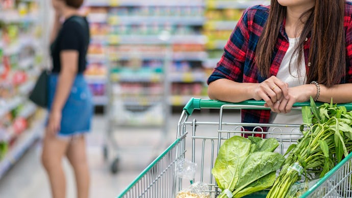 A woman leaning onto a shopping cart filled with $30 worth of groceries and veggies