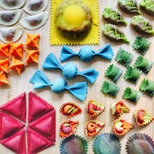 Rainbow pasta shaped like bows and ravioli spread across a table 