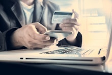 A man holding his phone and a 0% balance transfer credit card over his laptop