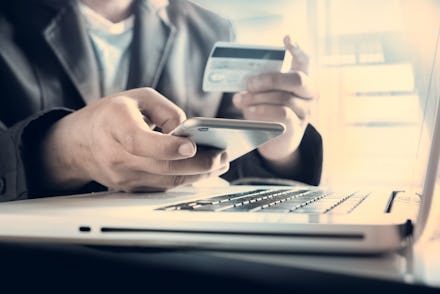 A man holding his phone and a 0% balance transfer credit card over his laptop