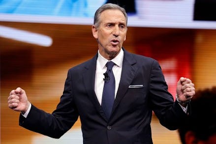 Howard Schultz, former Starbucks CEO in a black suit, black tie, and a white shirt speaking