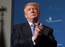 Donald Trump in a black suit, a white shirt and a blue tie clapping