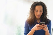 A woman holding her phone looking shocked at a dating app