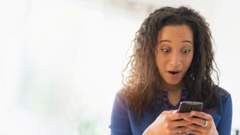 A woman holding her phone looking shocked at a dating app