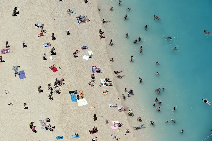 An aerial view of a crowded beach with people sunbathing and swimming in the sea