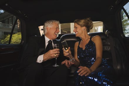 An older couple drinking champagne in the back of a limo while laughing together