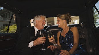An older couple drinking champagne in the back of a limo while laughing together