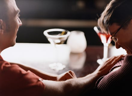 Two men who are dating sitting at a bar, and laughing with two drinks in front of them