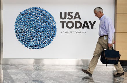 A man walking past a building with a large USA TODAY poster on a wall