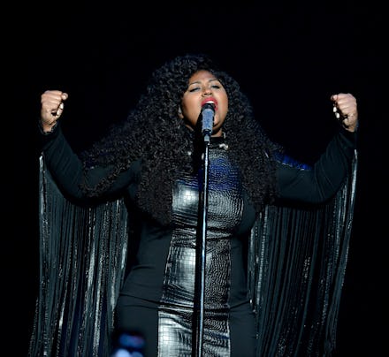 Jazmine Sullivan wearing a black leather dress with cape while performing on stage