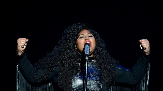 Jazmine Sullivan wearing a black leather dress with cape while performing on stage