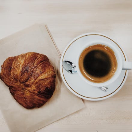 A croissant on a beige napkin and a cup of coffee