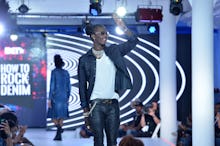 Young Thug walking the runway and waving in a denim jacket and jeans, with a white tee