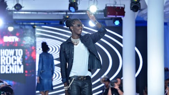 Young Thug walking the runway and waving in a denim jacket and jeans, with a white tee