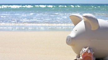 A piggy bank at the beach next to a conch