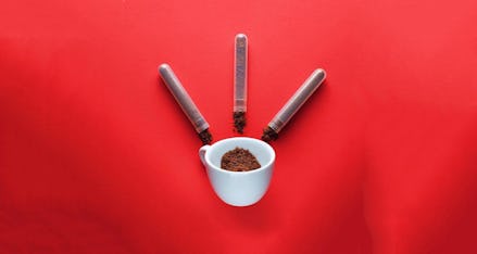 Three small tubes and a white mug with instant coffee in it on a red surface