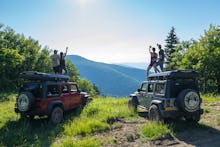 Two couples jumping on their jeeps in nature at the adult summer camp