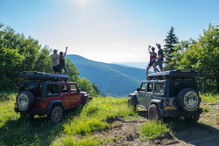 Two couples jumping on their jeeps in nature at the adult summer camp