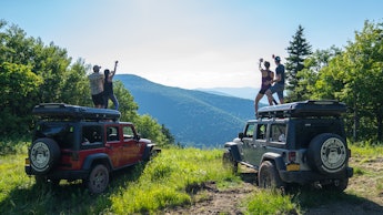 Two couples jumping on their jeeps in nature at the adult summer camp