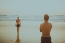 A man watching another man walk towards him at the beach