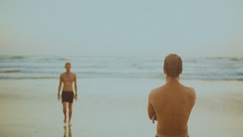 A man watching another man walk towards him at the beach