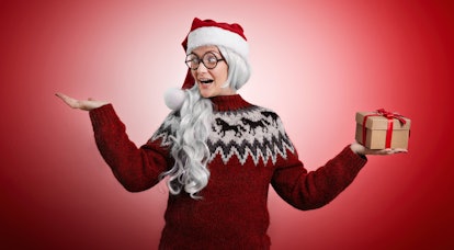 A girl wearing a red old school sweater and a Santa cap and wig and holding a small gift box