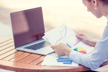 A woman using her laptop and looking at stock market paper charts