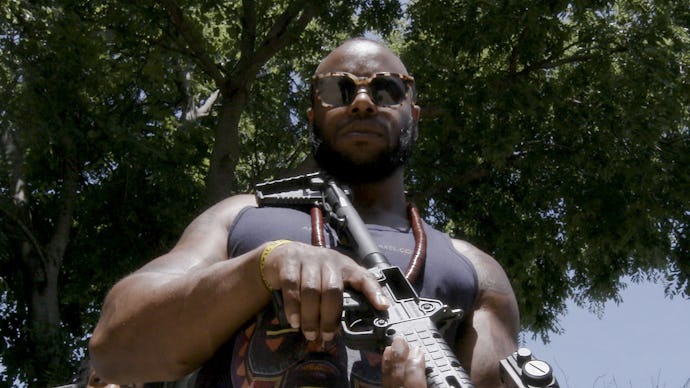 A man in a black tank top holding a gun while looking down