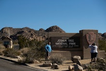 Two people stand in front of the sign for joshua tree national park and take a picture