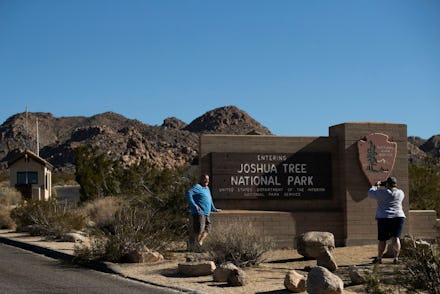 Two people stand in front of the sign for joshua tree national park and take a picture