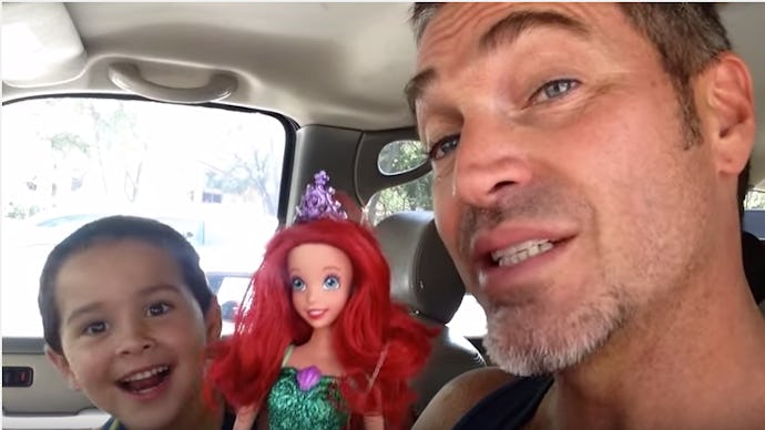 A dad sitting in a car next to his son, who is holding a 'Little Mermaid' doll