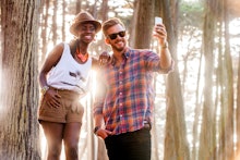 A woman in a white shirt and brown pants, and a man in a red-blue shirt and denim jeans taking a sel...