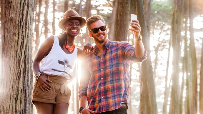 A woman in a white shirt and brown pants, and a man in a red-blue shirt and denim jeans taking a sel...