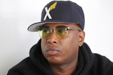 Talib Kweli wearing a black hat with an X on it and yellow glasses