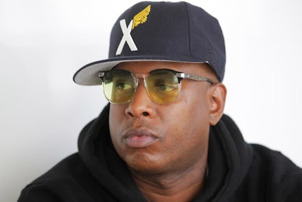 Talib Kweli wearing a black hat with an X on it and yellow glasses