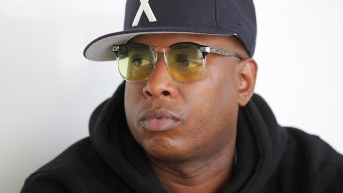 Talib Kweli wearing a black hat with an X on it and yellow glasses