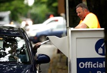 A man working a drive by voting booth and a person in a car handing over their ballot 