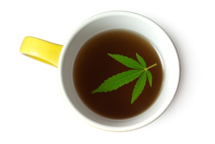 A white-yellow mug with marijuana tea and a large marijuana leaf on top of the tea
