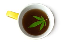 A white-yellow mug with marijuana tea and a large marijuana leaf on top of the tea